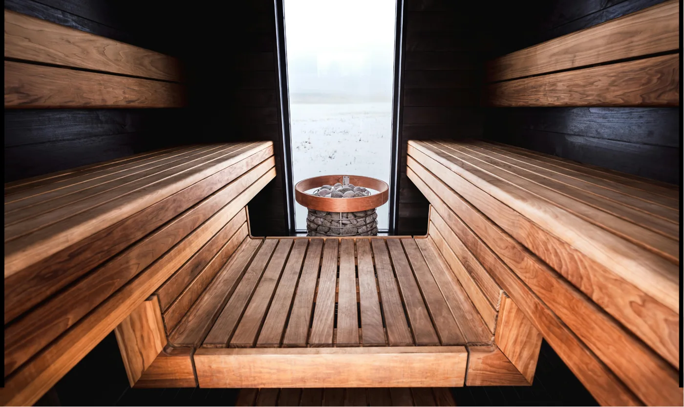 Wooden sauna benches facing a stove and a window onto a snowy landscape.