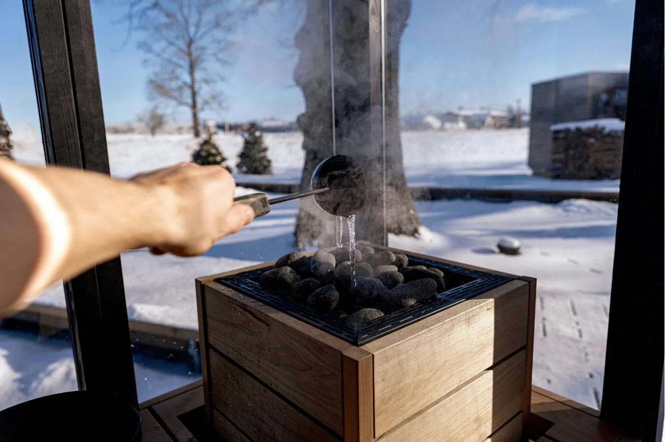 Water being poured over sauna stones, with snow visible through the window.