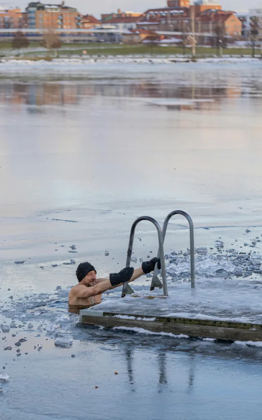 A winter swimmer holding the ladder beside an opening in the ice.